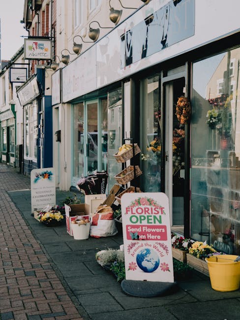 The exterior of South Ruislip Florist shows a storefront with large glass windows and a white sign indicating the shop is open, promoting flower delivery and floral gifts. Outside, there are several c