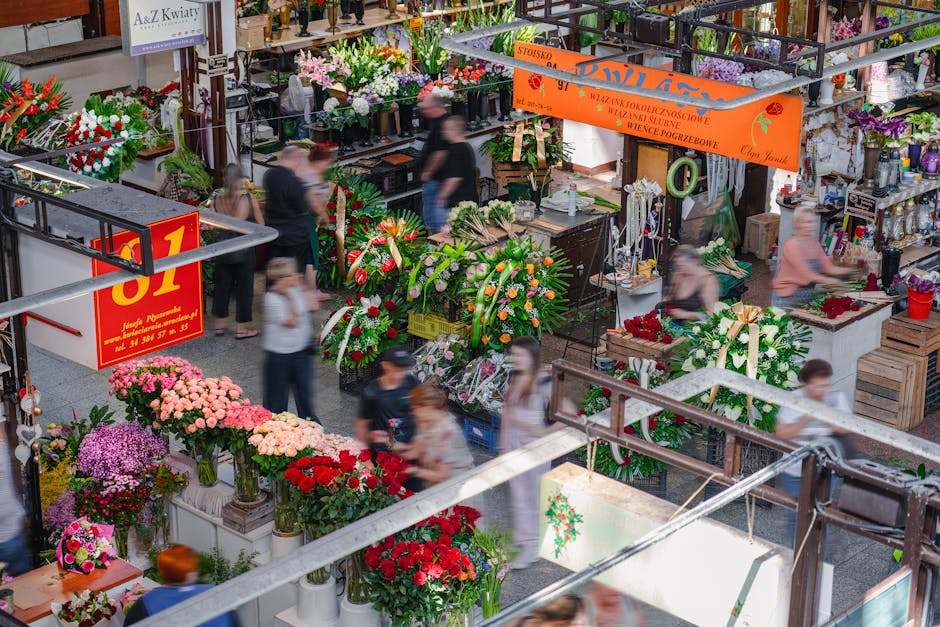 A vibrant flower market with an assortment of fresh floral arrangements and bouquets, featuring pink, red, purple, and white blooms organized in vases and containers. The flowers include roses, chrysa